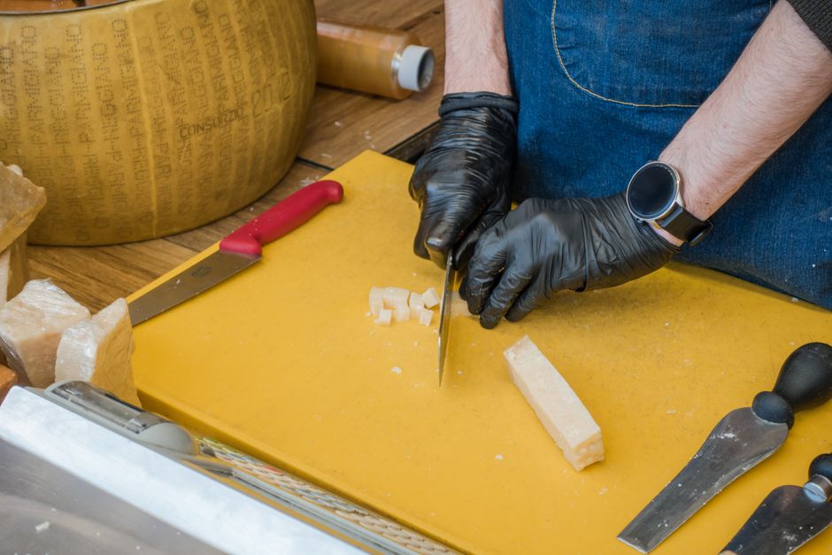 Person cutting Parmigiano-Reggiano cheese on a yellow board with various tools. Perfect for culinary themes.
